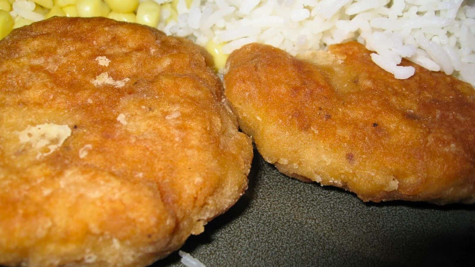 Image shows two Salmon Patties on a green plate with rice and corn.