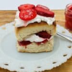 A piece of biscuit with strawberries and whipped cream on a white plate.