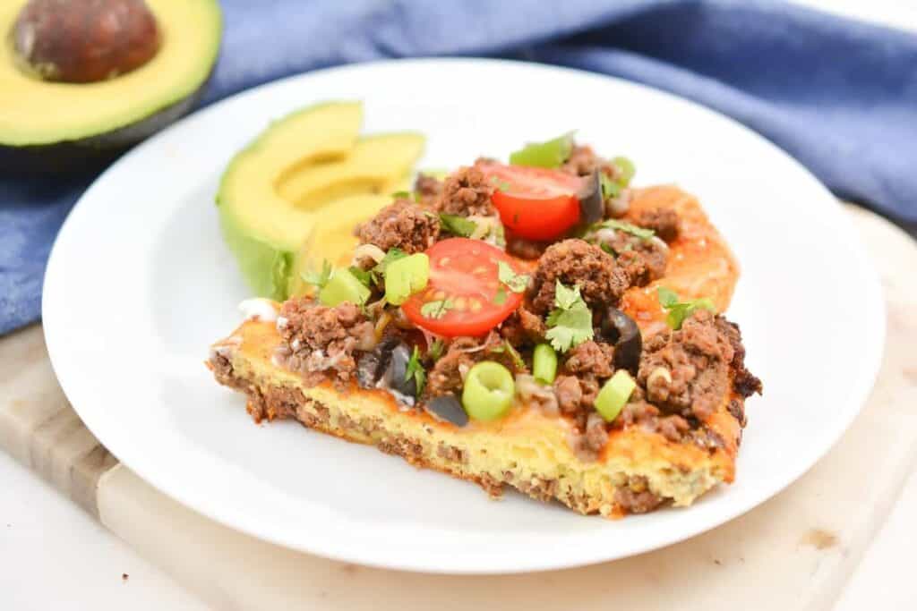 A slice of meat and avocado breakfast pizza on a plate.