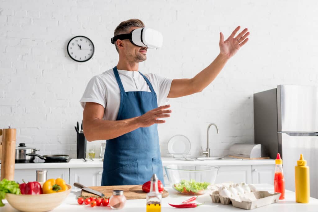 A man in an apron is preparing food in a kitchen with a virtual reality headset.