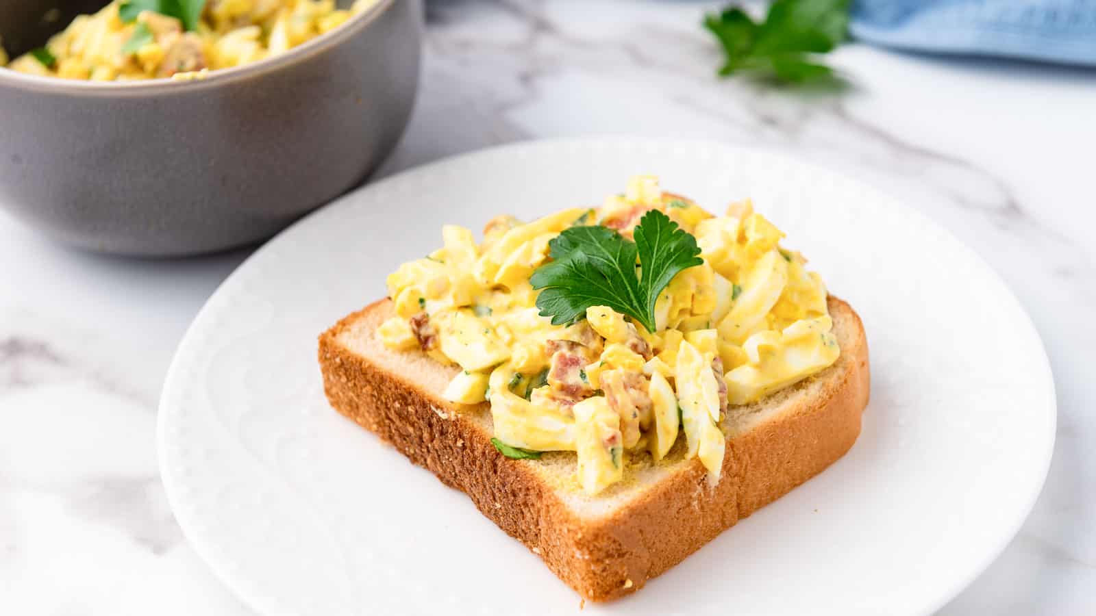 An egg salad sandwich on a slice of bread with parsley.