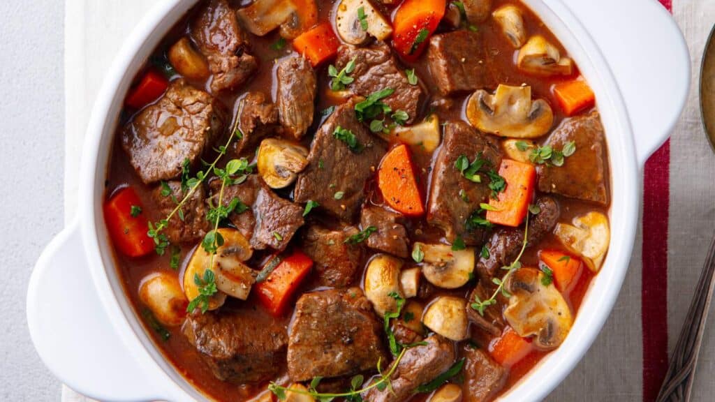 Beef stew with mushrooms and carrots in a white bowl.