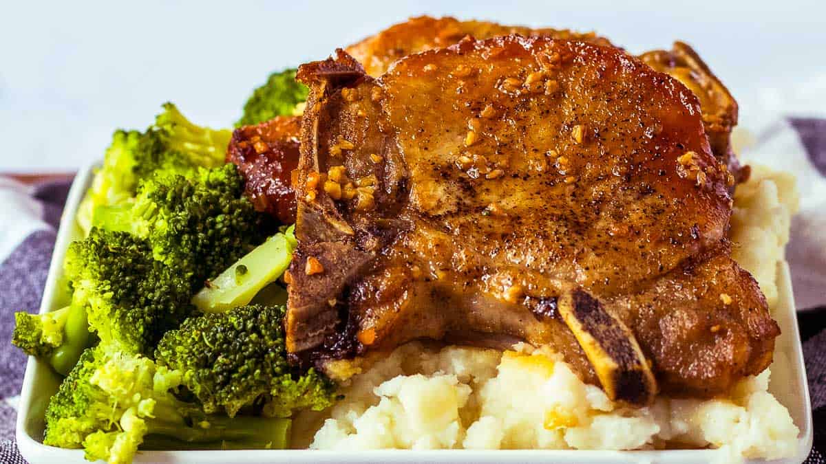 Pork chops on a plate with broccoli and mashed potatoes.