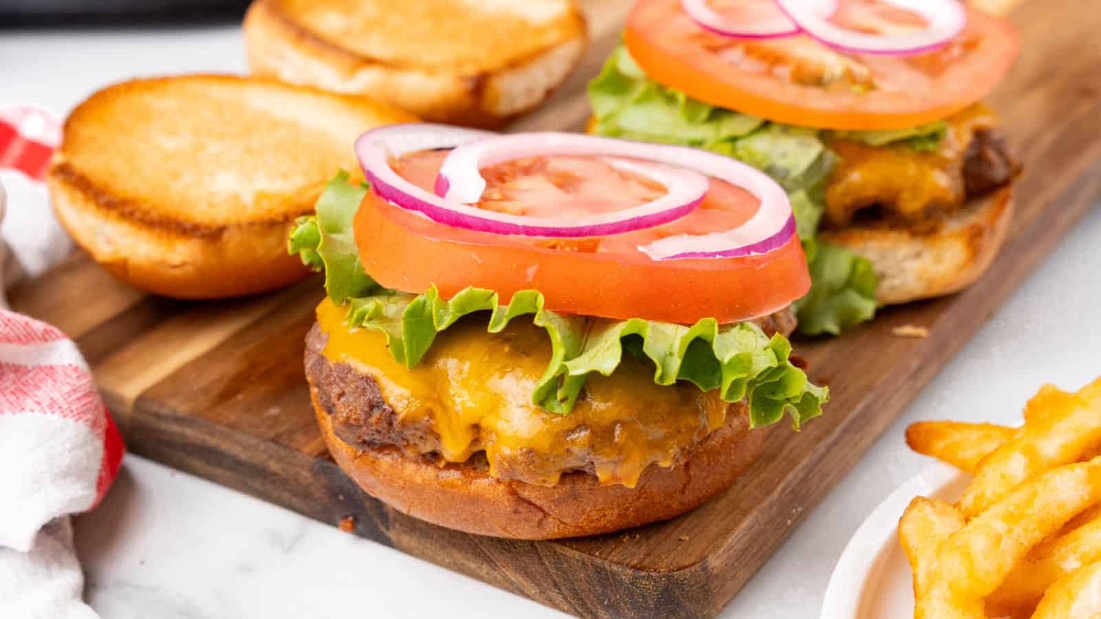 Burgers and fries on a wooden cutting board.