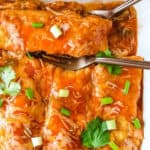 Mexican enchiladas in a white dish with a fork.
