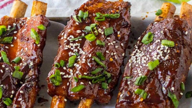 A tray of ribs with sesame seeds and green onions.