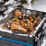 A composting bin full of food scraps in the snowy winter.