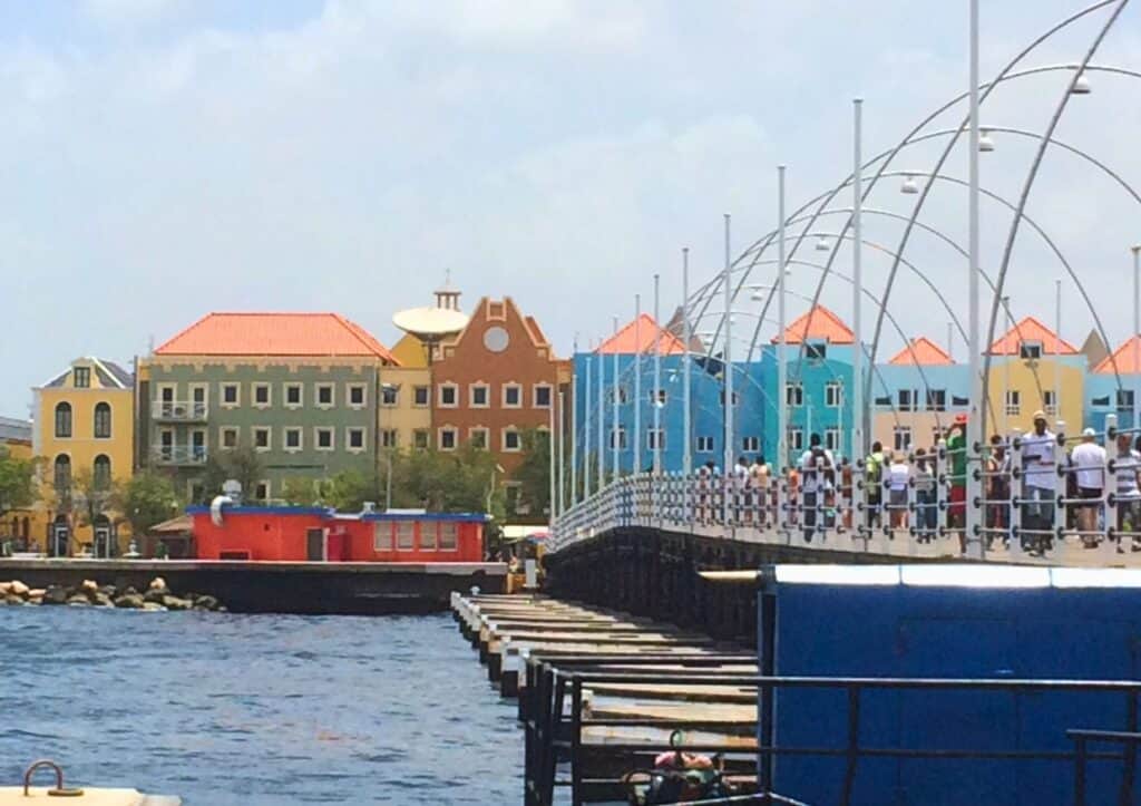 A group of people walking on willemstad over water.