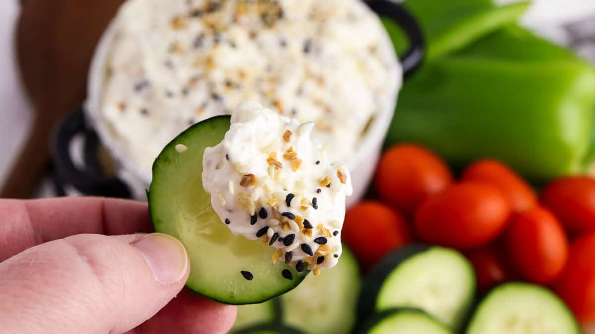 A bowl of dip with cucumbers, tomatoes and sesame seeds.