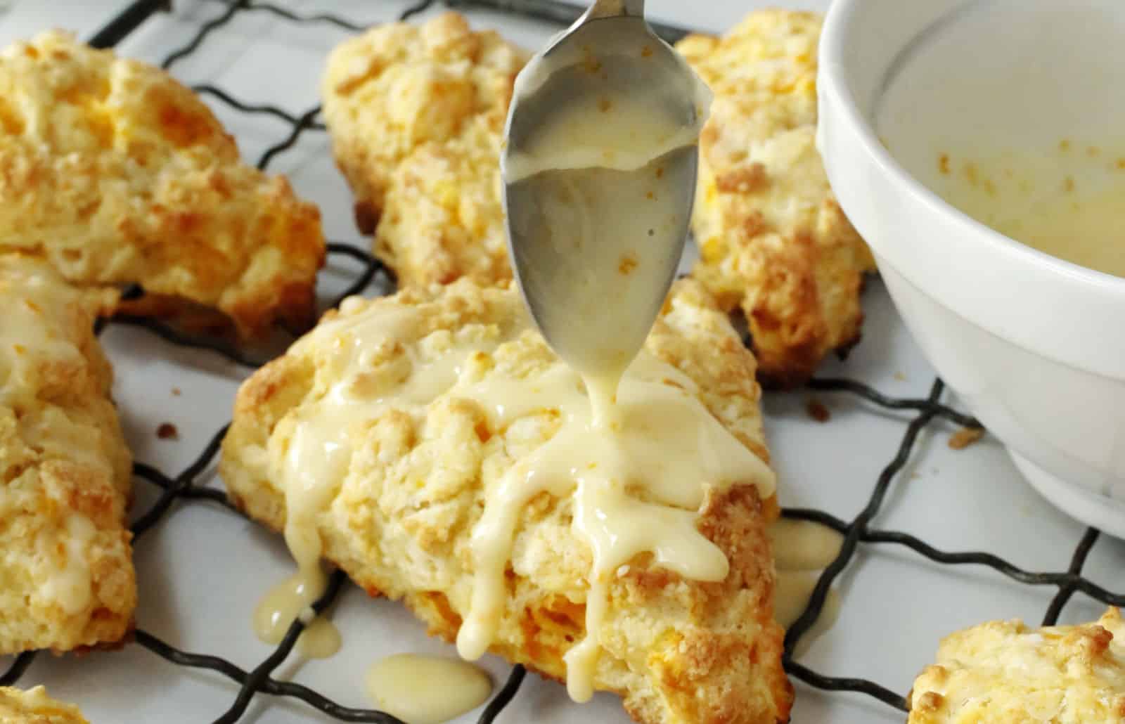 Scones being drizzled with icing on a cooling rack.