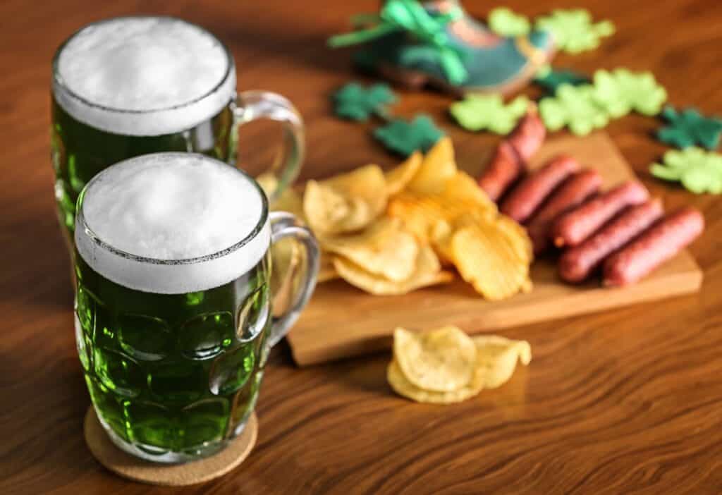 Two mugs of beer and chips on a wooden table.