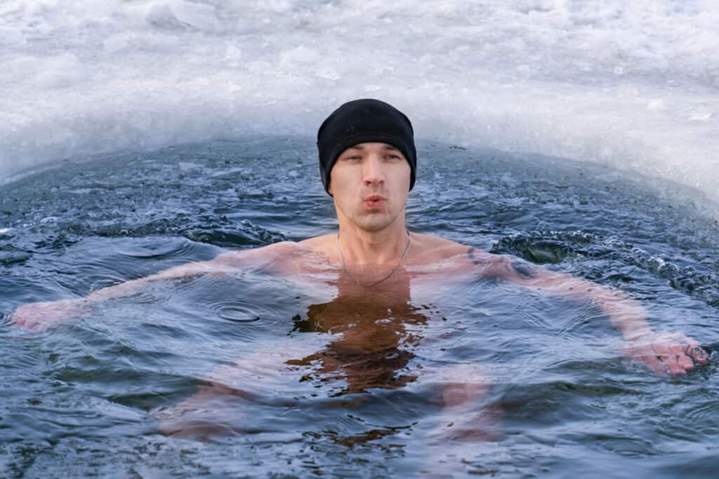 A man in a beanie is practicing cold water immersion therapy in an ice pool.