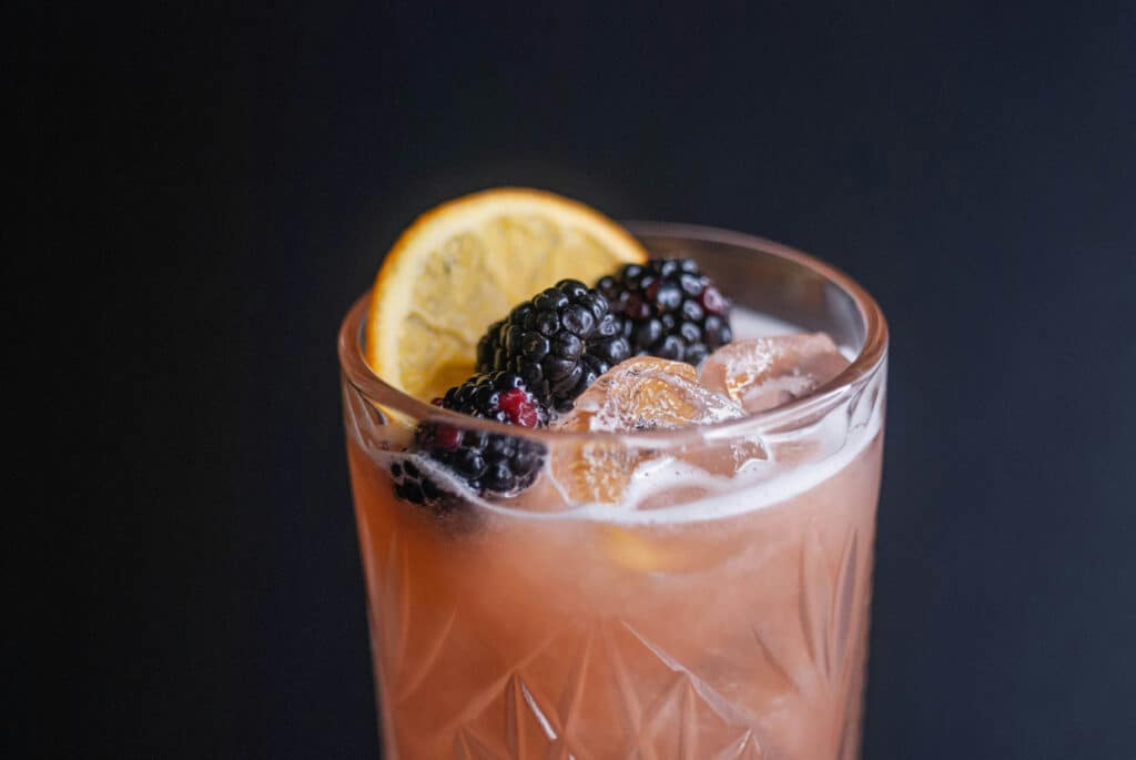 A cocktail with blackberries and ice in a glass.