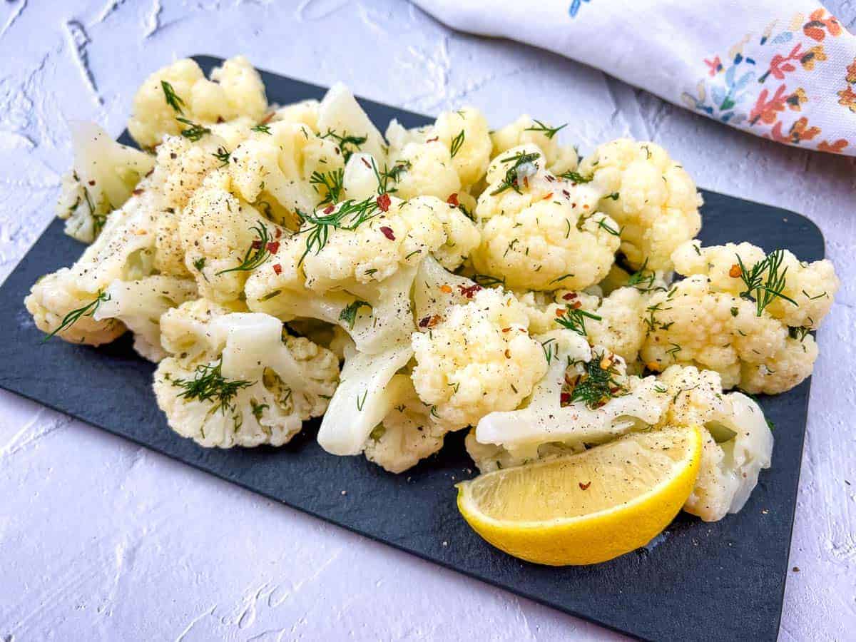 Cauliflower with lemon and dill on a black board.