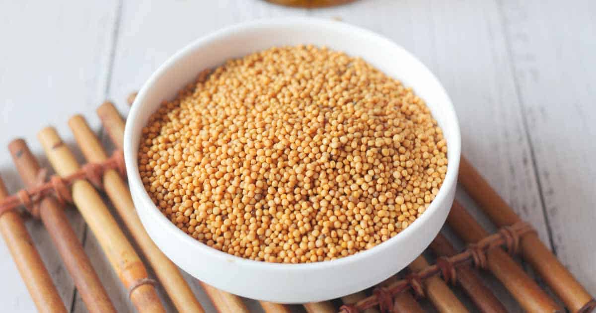 Mustard seeds in a bowl on top of a bamboo mat.