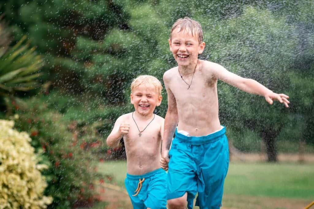 Two boys having an outdoor play by running in the water sprinkles.