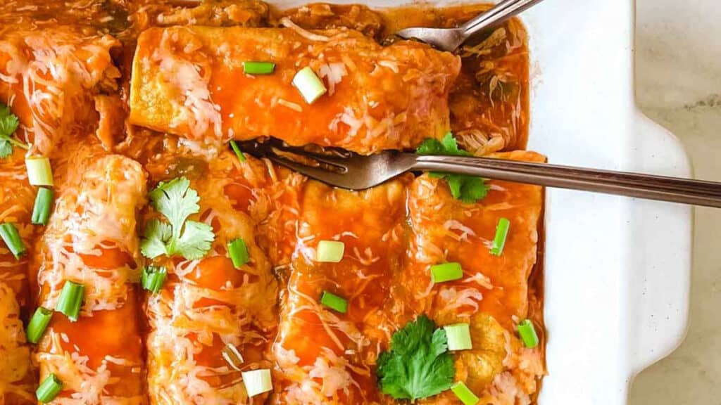 Mexican enchiladas in a white dish with a fork.