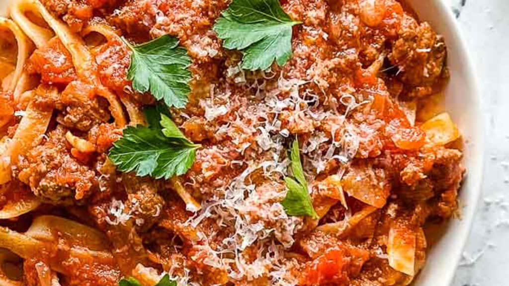 A bowl of pasta with meat sauce and parsley.
