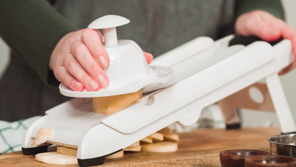 A person using a vegetable slicer on a cutting board.