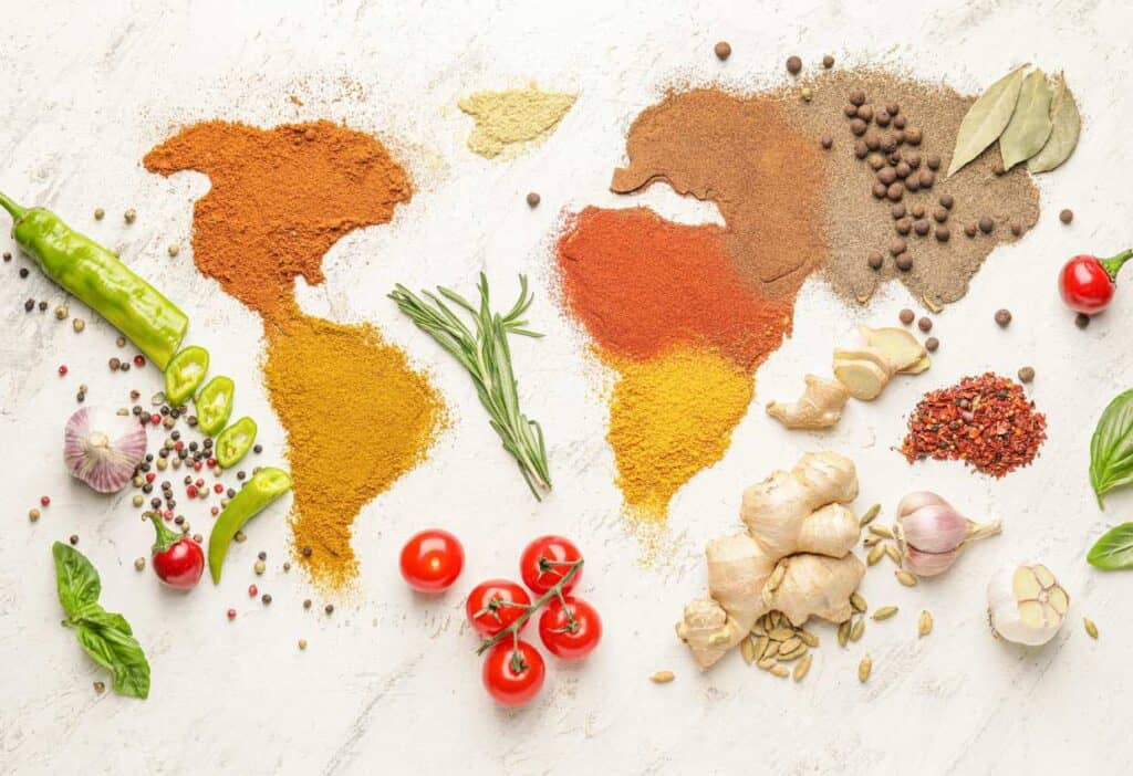 A world map showcasing various types of cuisines with a vibrant display of spices and herbs on a white background.