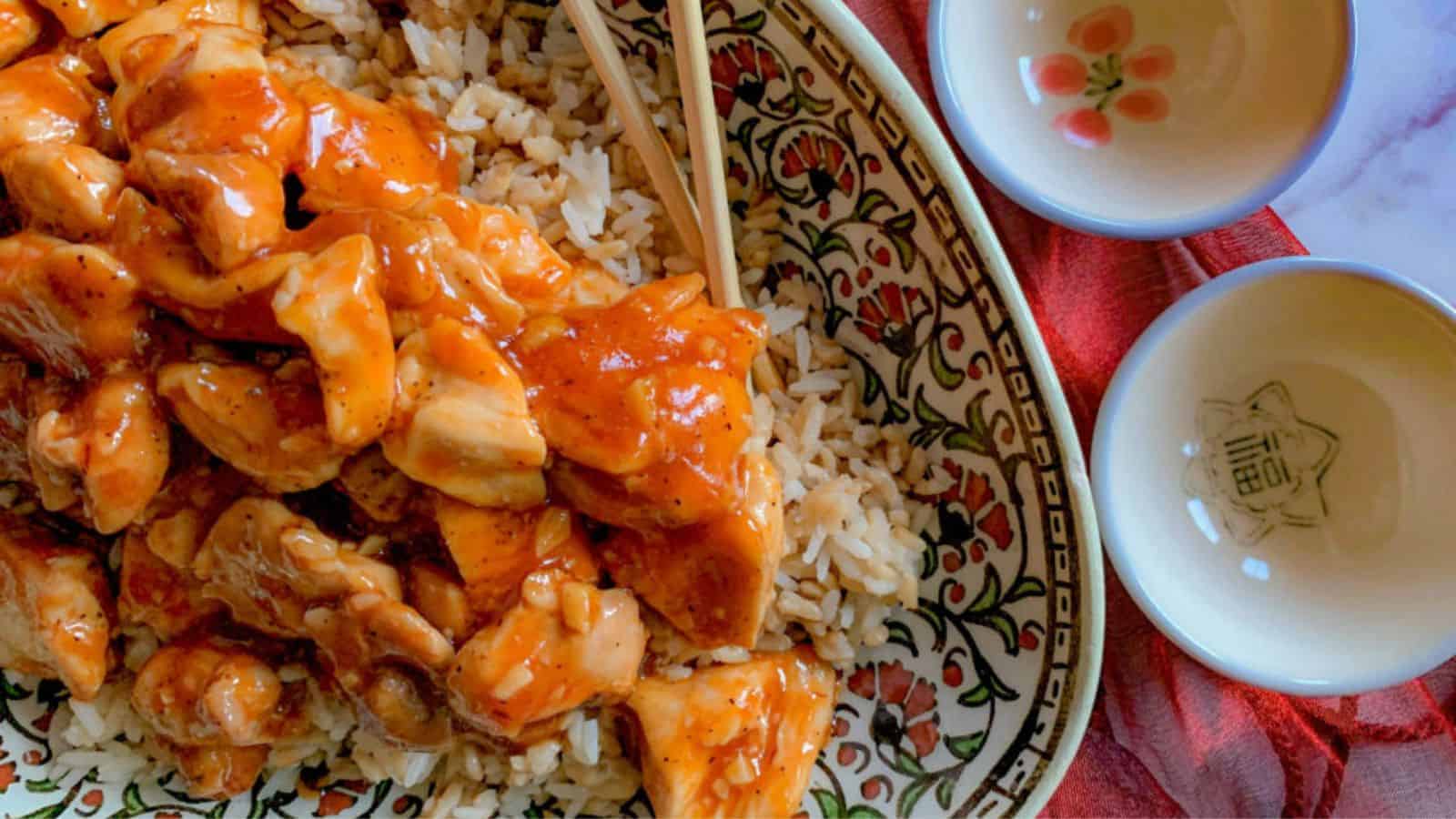 A plate of Chinese honey chicken over rice with chopsticks.