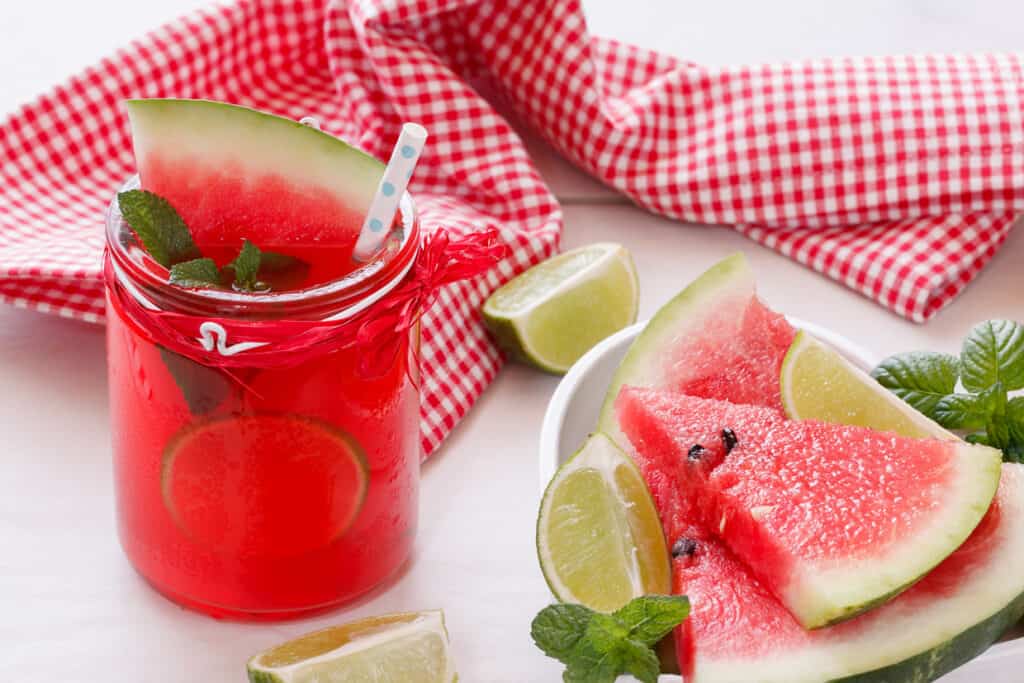 A refreshing watermelon drink garnished with mint and simple syrup substitutes, served alongside fresh watermelon slices and lime wedges.