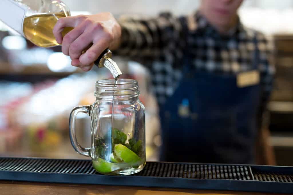 Bartender pouring simple syrup substitutes into a mason jar with lime and mint for a cocktail.