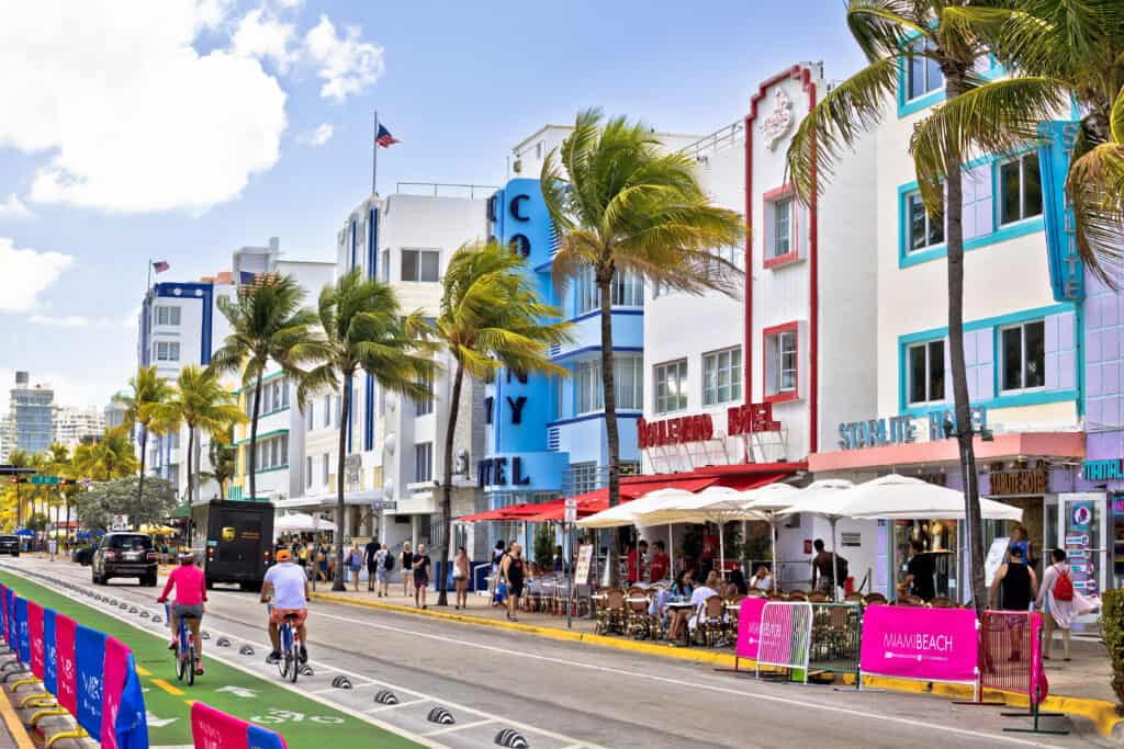 Colorful art deco buildings line a bustling street with pedestrians and cyclists in miami beach.