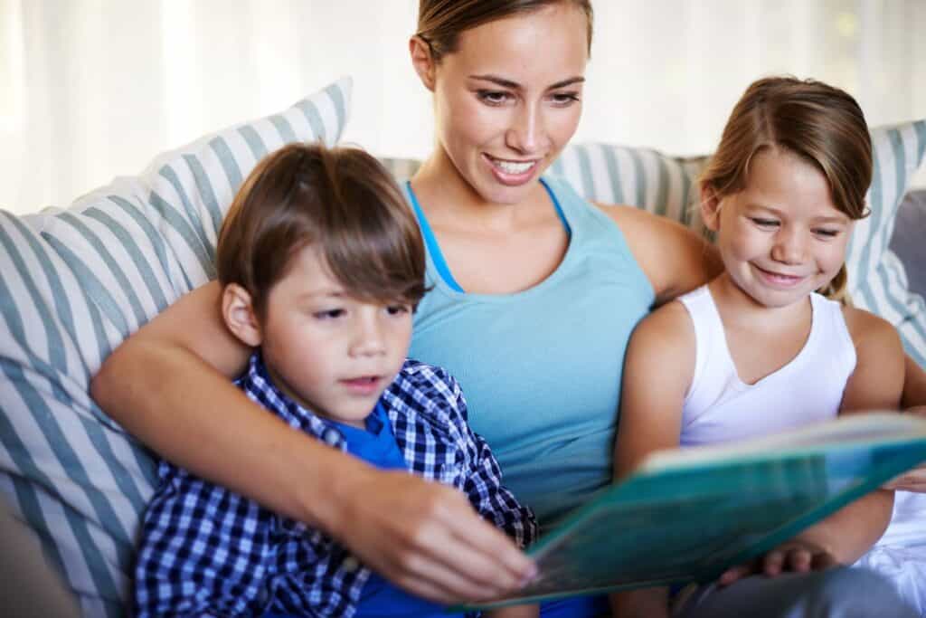 A woman is reading a book to her children on a couch.