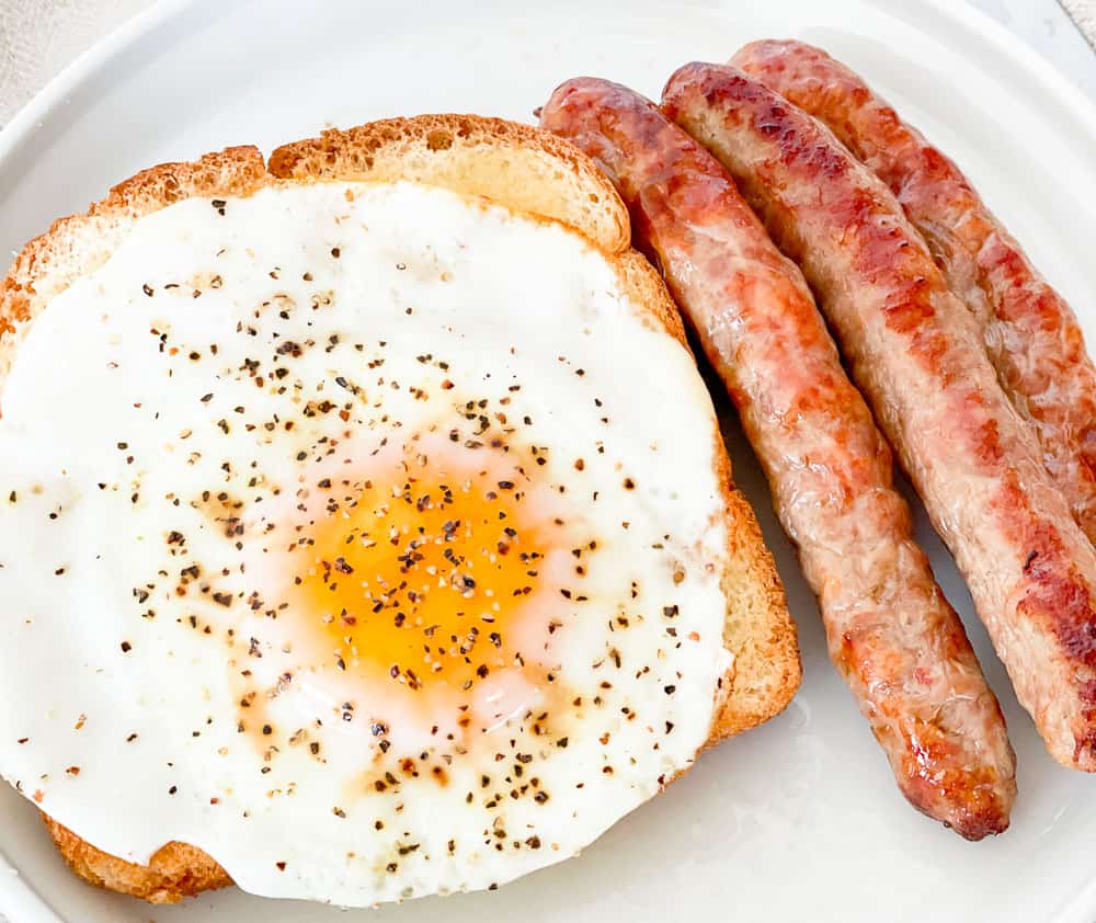 Plate with a fried egg on toast and three sausages.