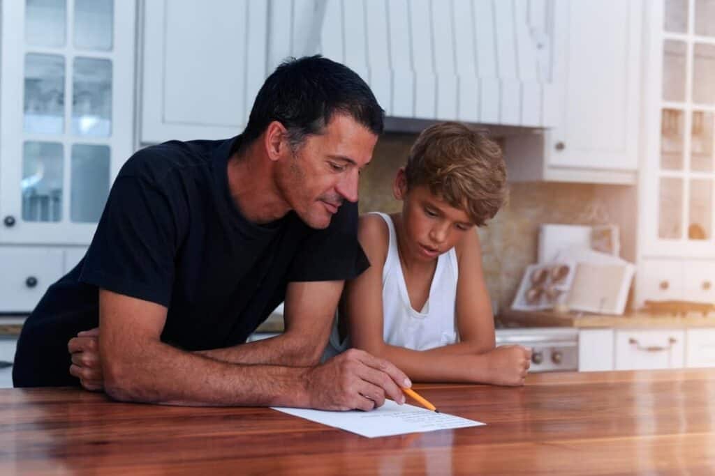 A father and son working on a paper in the kitchen.