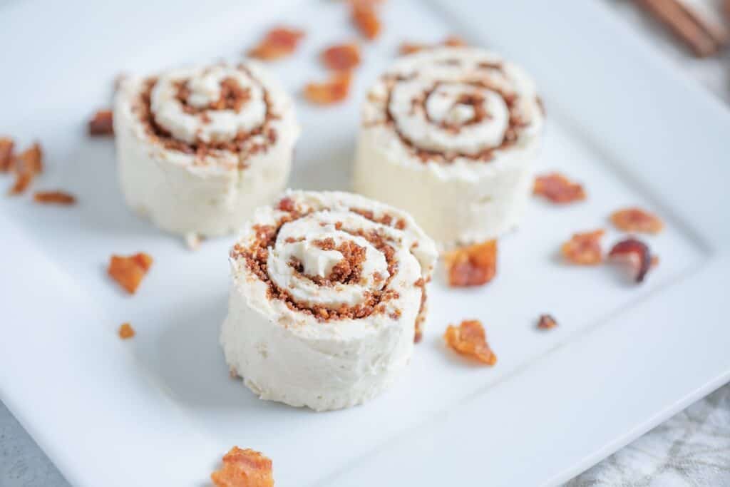 Three cinnamon rolls with cream cheese frosting served on a white plate, sprinkled with cinnamon and pieces of what appears to be dried fruit.