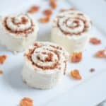 Three cinnamon rolls with cream cheese frosting served on a white plate, sprinkled with cinnamon and pieces of what appears to be dried fruit.