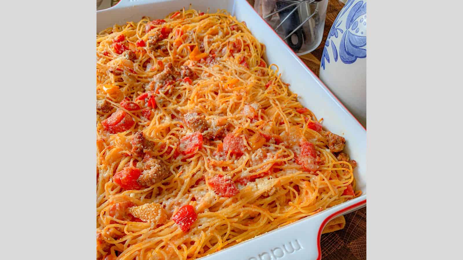 A spaghetti noodles casserole in a baking dish with peppers, tomatoes, and cheese.