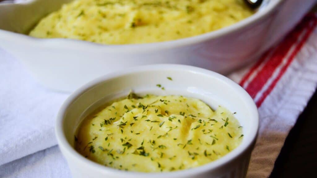 Baked mashed potatoes garnished with herbs in a white ramekin and casserole dish.