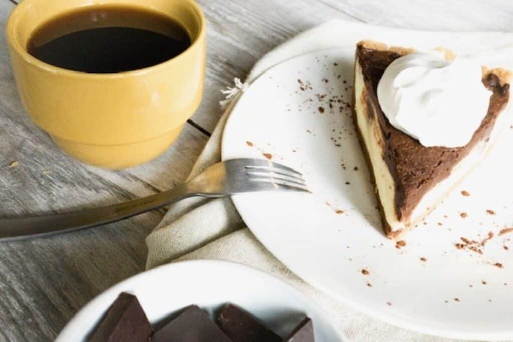 A slice of chocolate pie with whipped cream on a plate, a cup of coffee, and pieces of chocolate on the side.