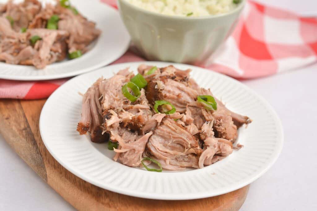 Shredded pork on a white plate garnished with green onions, with rice in the background.