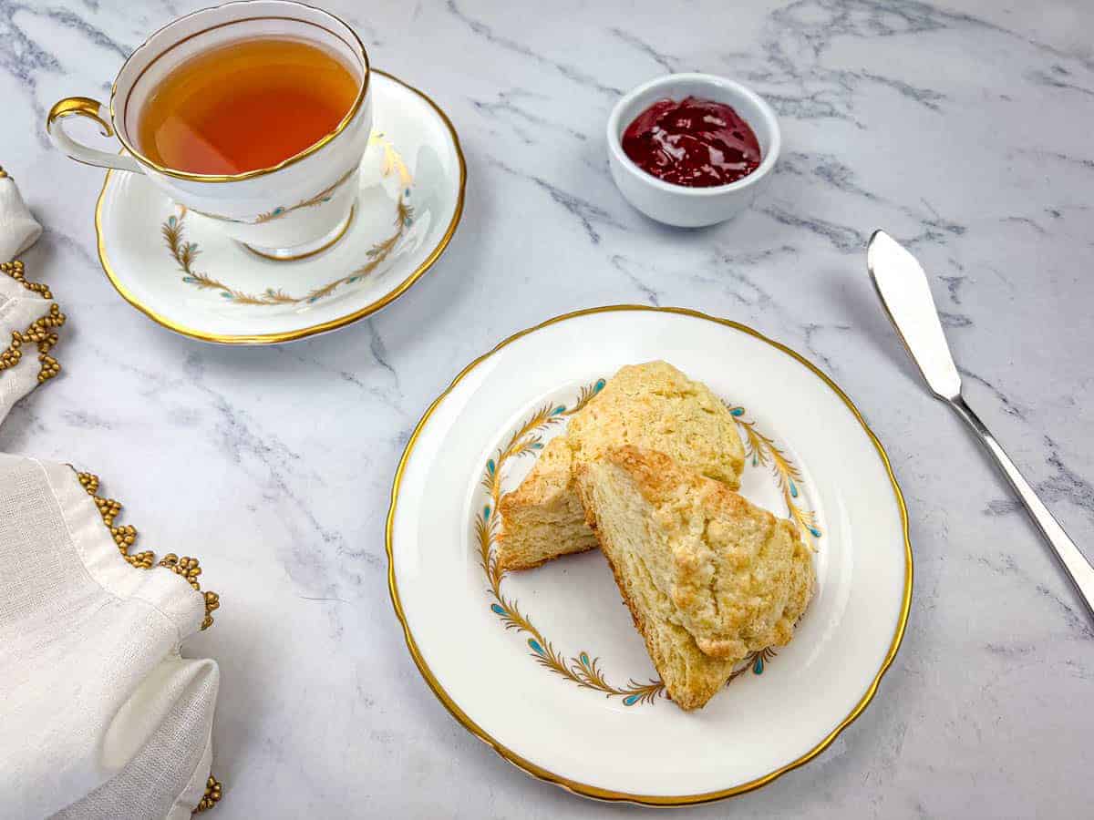 Two butter scones on a plate with a cup of tea on a marble surface.