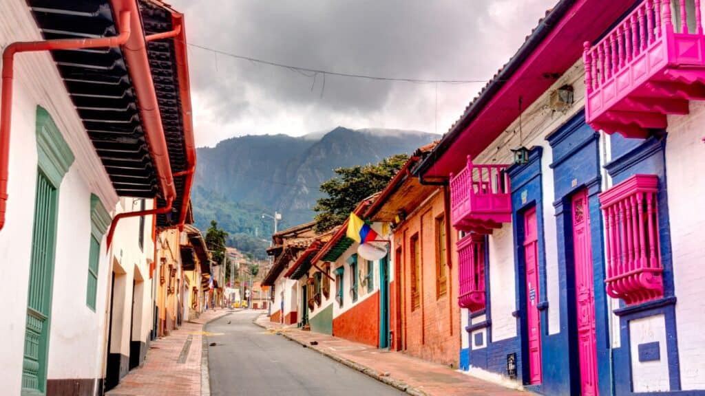 A colorful street with vibrantly painted houses in a traditional latin american town, under a cloudy sky with mountains in the background.