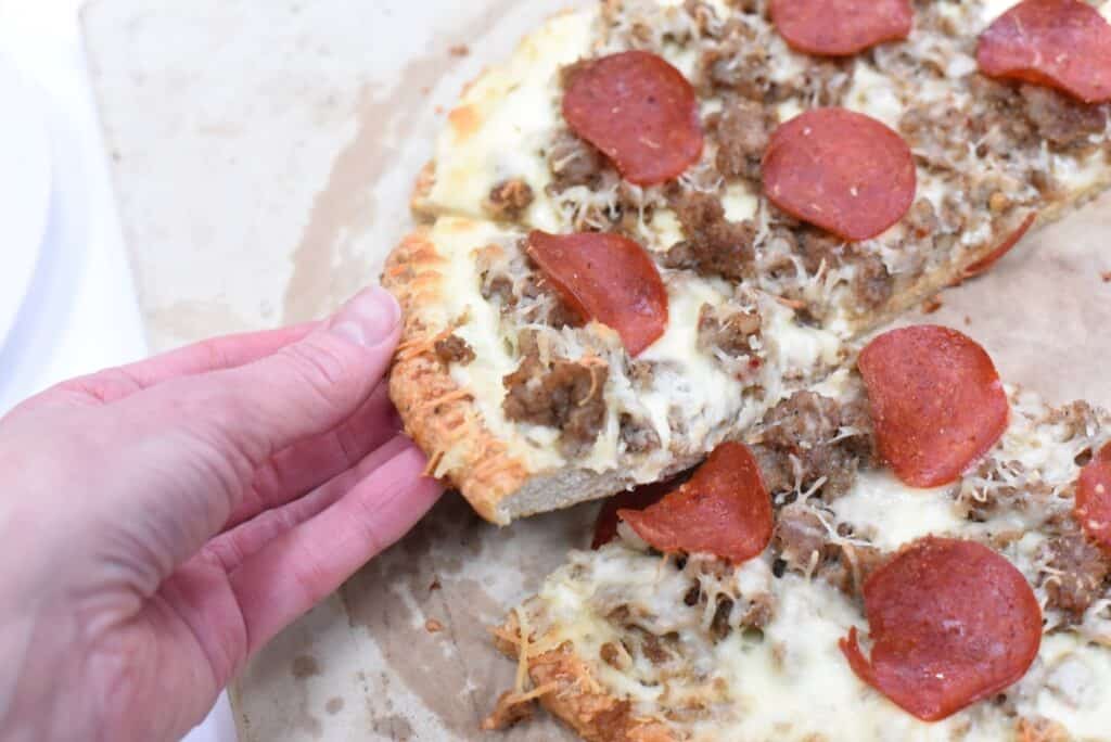 A person holding a slice of pepperoni and ground beef pizza.