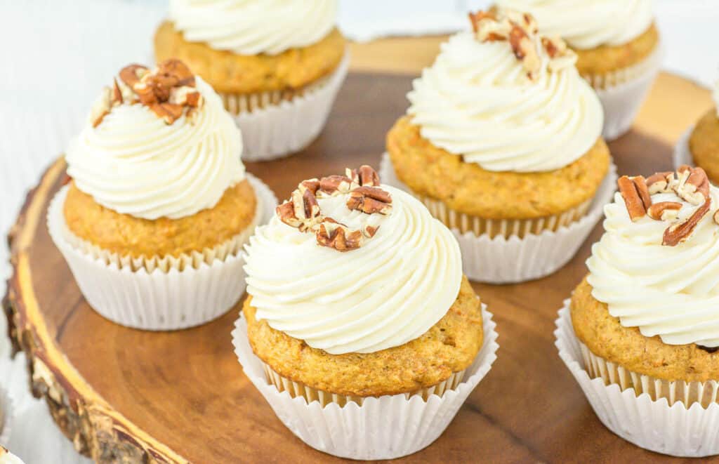 Freshly baked cupcakes with creamy frosting and pecan topping displayed on a wooden surface.