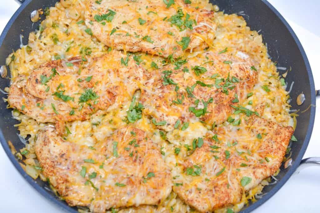 Cheesy chicken dish in a skillet, garnished with herbs.