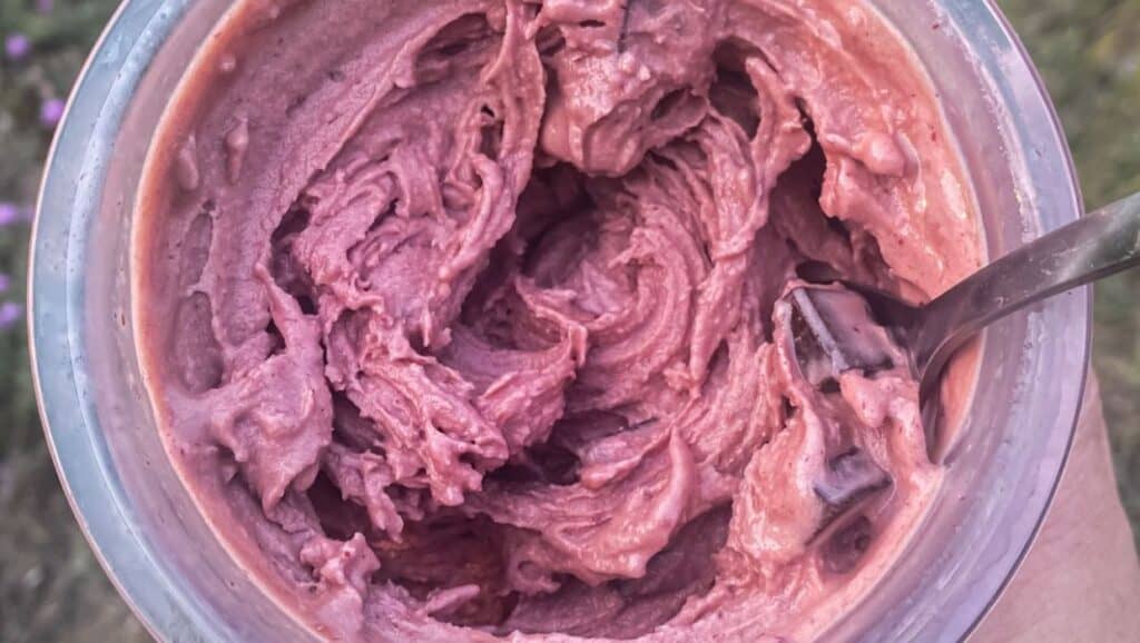 A close-up view of a purple, creamy substance, possibly a dessert like ice cream or smoothie, in a clear container with a spoon.