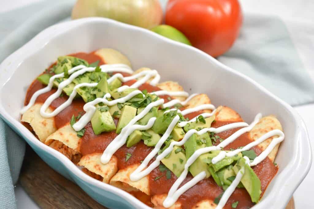 A dish of enchiladas topped with red sauce, sour cream, and diced avocado.