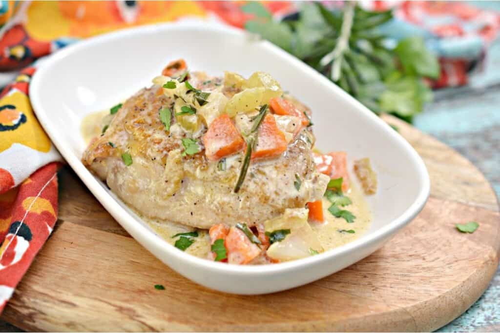 Seared chicken breast topped with a creamy sauce and diced vegetables on a white dish.