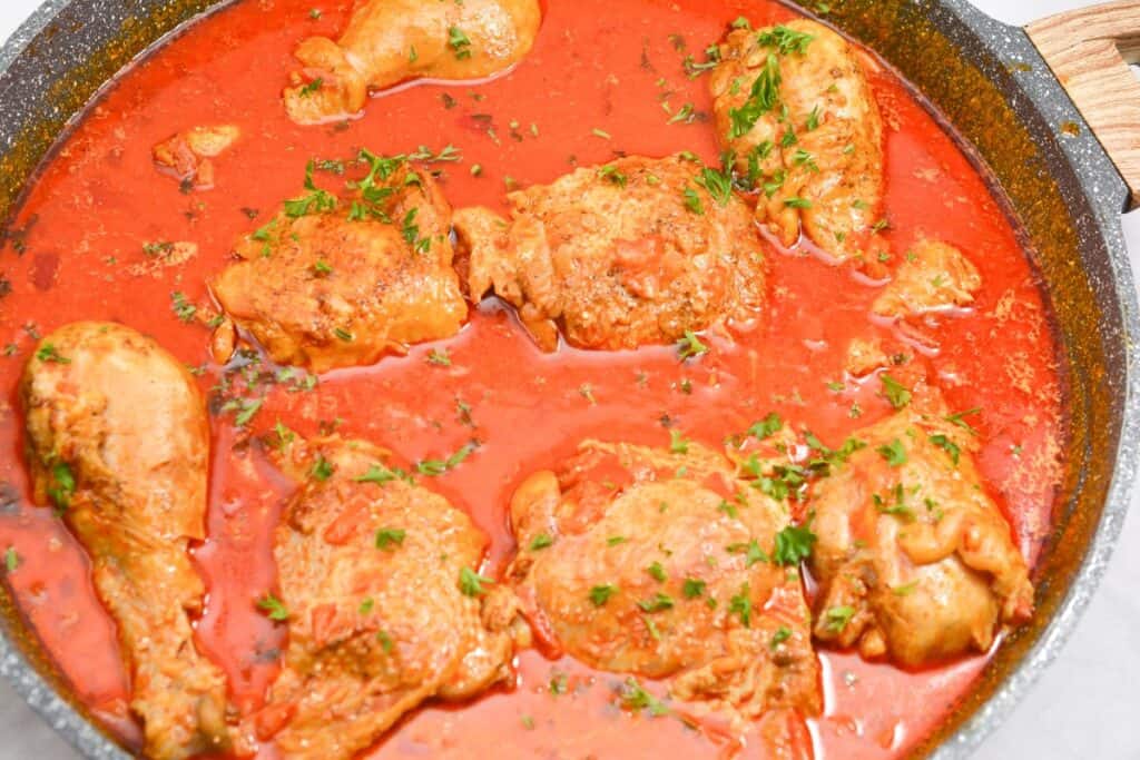 Chicken pieces simmering in tomato sauce, garnished with herbs.