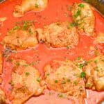 Chicken pieces simmering in tomato sauce, garnished with herbs.
