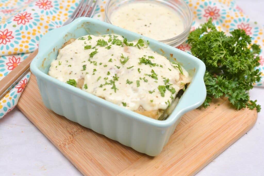 Baked dish topped with creamy sauce and fresh herbs, served with extra sauce on the side.