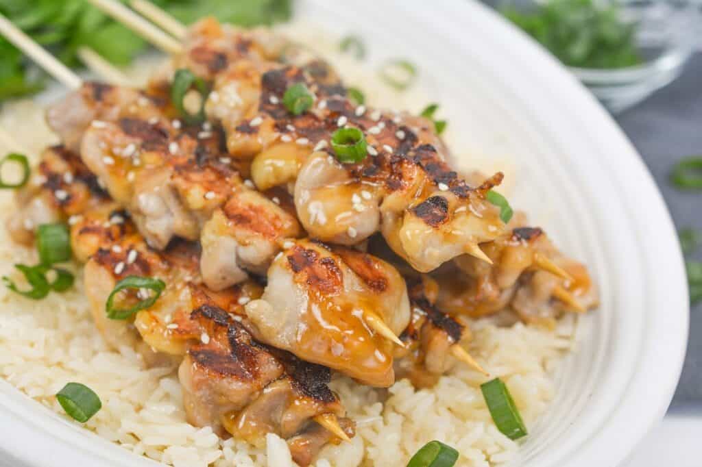 Grilled chicken skewers, garnished with sesame seeds and chopped green onions.