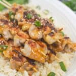 Grilled chicken skewers, garnished with sesame seeds and chopped green onions.